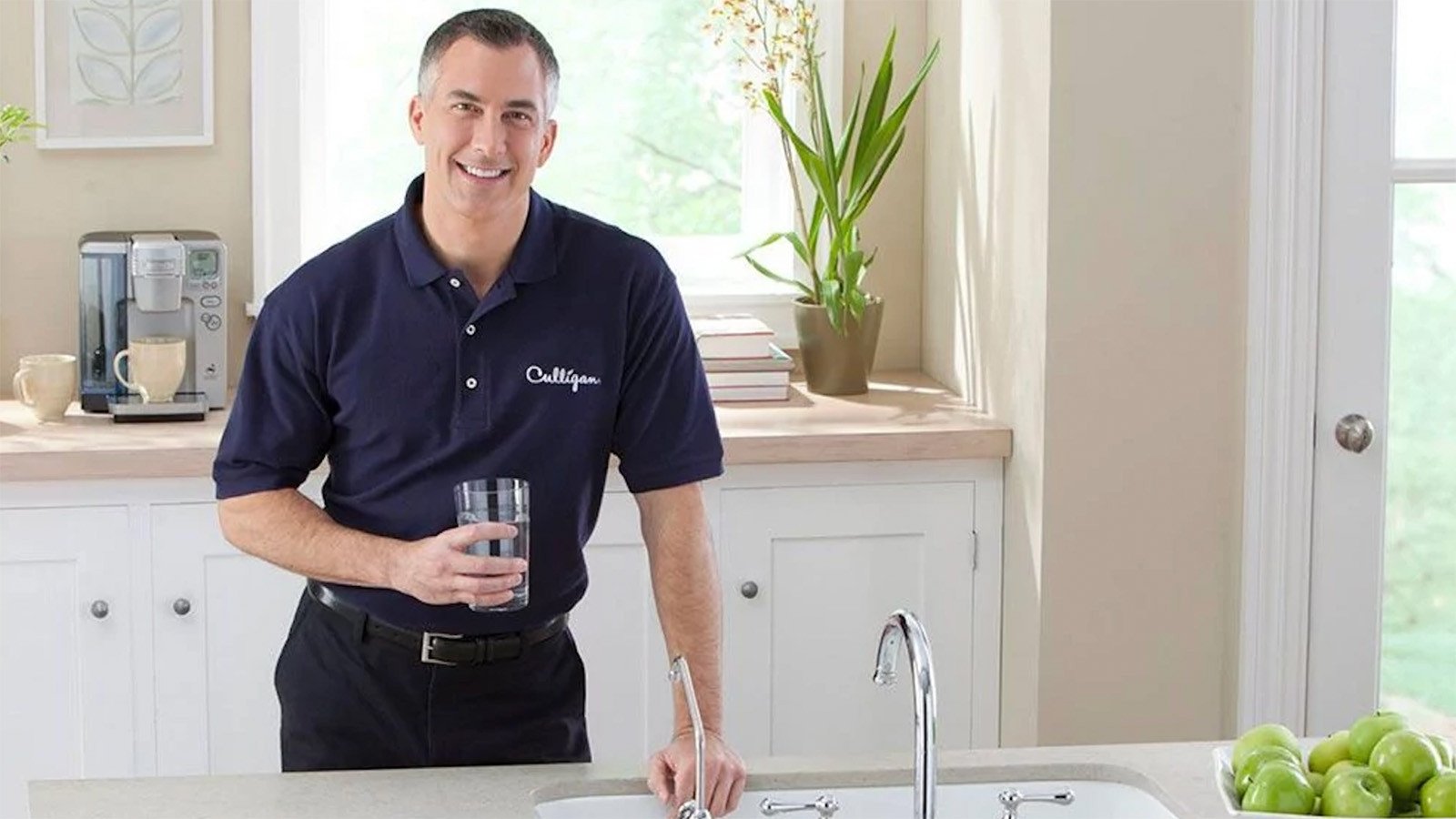 Culligan expert holding a glass of water by kitchen sink