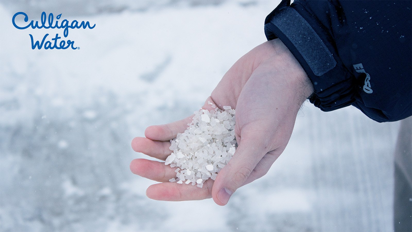 Hand holding a small amount of salt on a snowy sidewalk