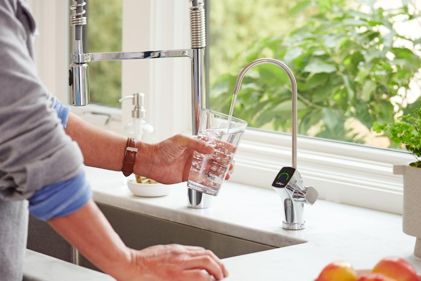 Person filling a glass with water at a kitchen sink